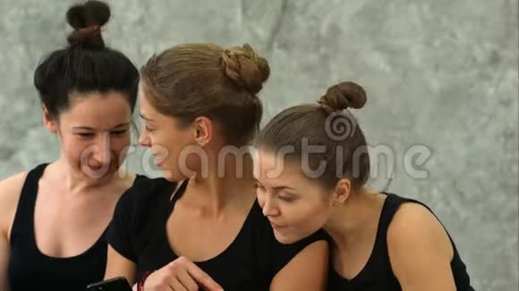 三位年轻女性在瑜伽课锻炼后使用智能手机上网视频的预览图