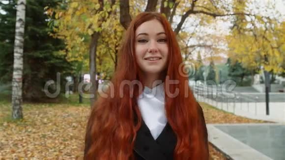一个留着红色头发的女孩站在公园里落叶下视频的预览图