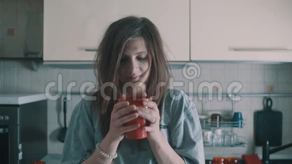 一个漂亮的女孩早上在厨房里喝着红色杯子里的咖啡微笑着视频的预览图