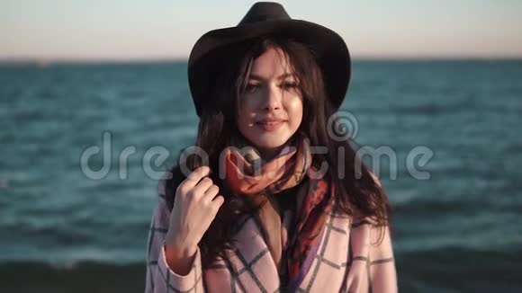 海洋背景上可爱女孩特写的肖像穿着秋装戴帽子的年轻女子在镜头前摆姿势微笑视频的预览图