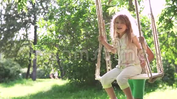 孩子们在夏天公园的秋千上荡秋千两个小妹妹在新鲜空气中玩耍姐姐摇摇她视频的预览图