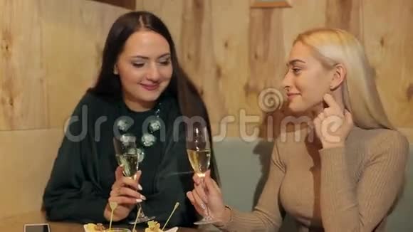 两个年轻女孩笑着坐在一家带着香槟的咖啡馆里视频的预览图