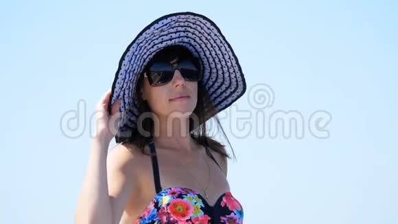 夏天大海一个美丽的年轻黑发女人的肖像穿着泳衣戴着太阳帽戴着太阳镜站在上面视频的预览图