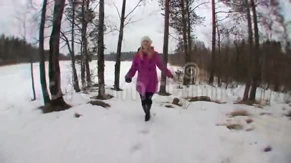 穿着粉红色外套的年轻金发女子在冬天的森林里奔跑视频的预览图