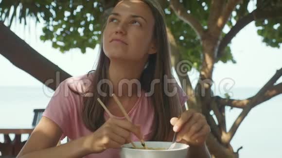 年轻女子在露天海滩咖啡馆用筷子吃面条汤视频的预览图