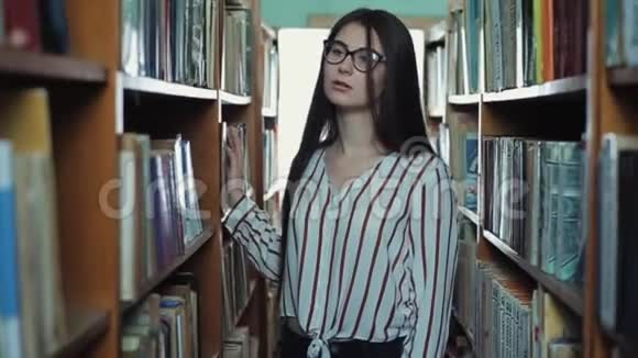 漂亮的小女孩留着长长的黑发在图书馆的书架之间视频的预览图