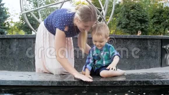 在公园的喷泉里欢快的幼儿男孩在喷水池里和年轻的妈妈玩耍视频的预览图