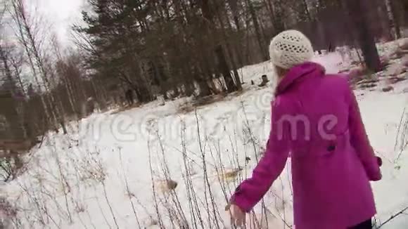 穿着粉红色外套的年轻女子在冬天的森林里散步触摸树枝视频的预览图