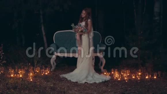 新娘拿着花束站在黑暗森林的沙发前点燃蜡烛视频的预览图