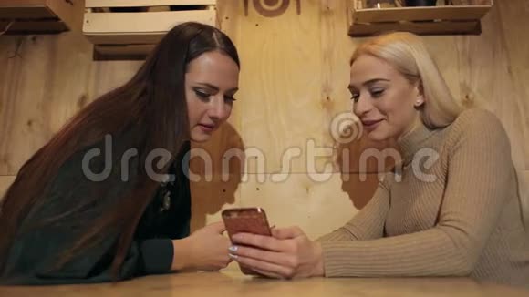 两个漂亮的女孩坐在咖啡馆里带着电话和微笑视频的预览图