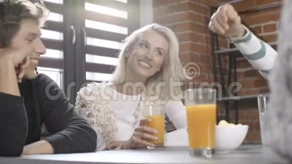 一群年轻的朋友围着桌子聊天在现代阁楼内部的休闲日里喝着健康的橙色饮料视频的预览图