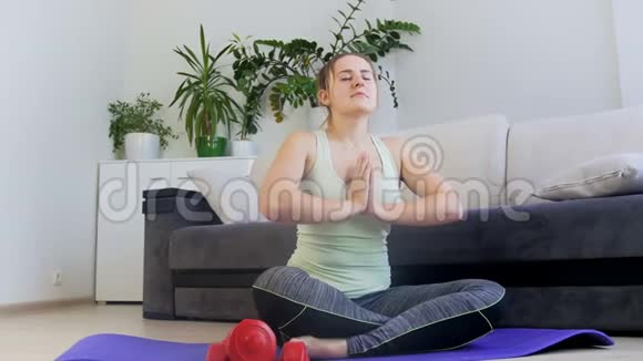 多莉4k镜头年轻女子坐在家里的健身垫上莲花瑜伽姿势视频的预览图