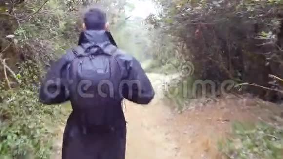 穿着雨衣的年轻人在旅行时走在树林里徒步旅行者带着背包在热带潮湿的森林里散步后续行动视频的预览图