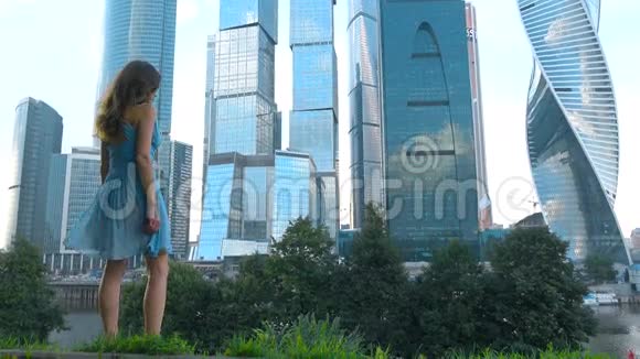 穿着蓝色裙子的苗条女孩看着俄罗斯莫斯科市的现代化摩天大楼4K镜头视频的预览图