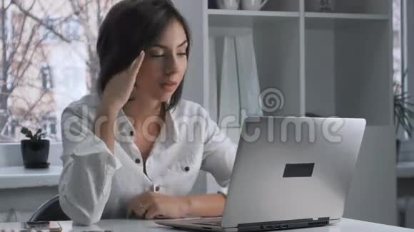 在办公室的笔记本电脑里工作的疲惫的女人视频的预览图