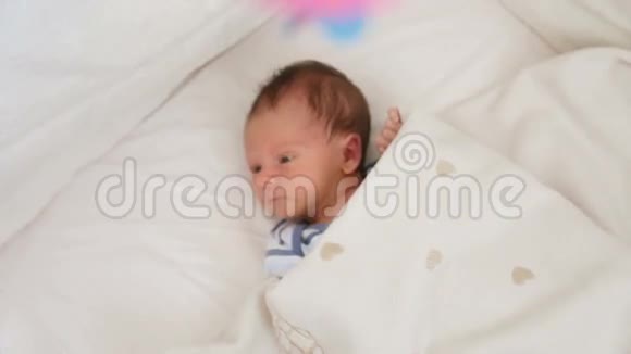 新生儿躺在婴儿床的毯子下用五颜六色的旋转移动视频的预览图
