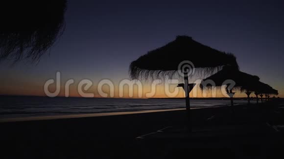 海滩上夕阳西下稻草伞的轮廓映衬在天空上视频的预览图