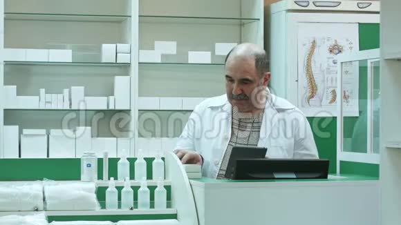 具有大胡子的高级药剂师在药房检查药品时使用平板电脑视频的预览图