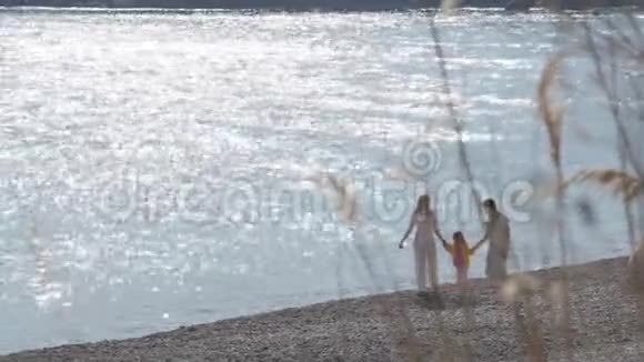 快乐的父母和女儿在阳光明媚的日子里走在海岸上视频的预览图