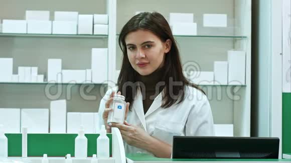 一位年轻的年轻药剂师拿着一瓶药站在药店看着摄像机视频的预览图