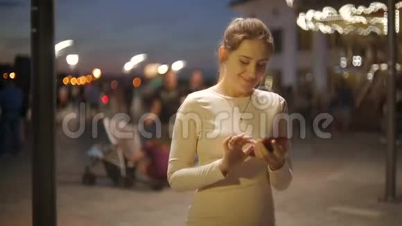 晚上在拥挤的街道上使用智能手机的漂亮年轻女子的头部镜头视频的预览图