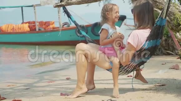 妈妈和她可爱的小女儿在沙滩吊床上玩视频的预览图