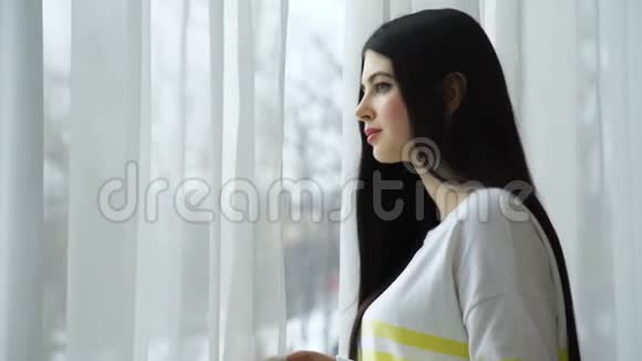美丽的年轻女子望着窗户等待视频的预览图