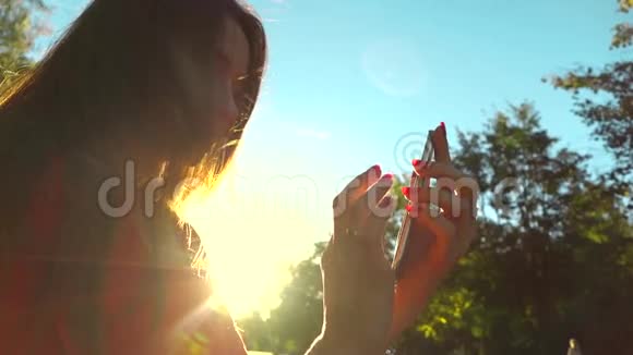 美丽的女孩穿着红色的裙子在公园里用手机温暖的夕阳颜色慢镜头中镜头视频的预览图