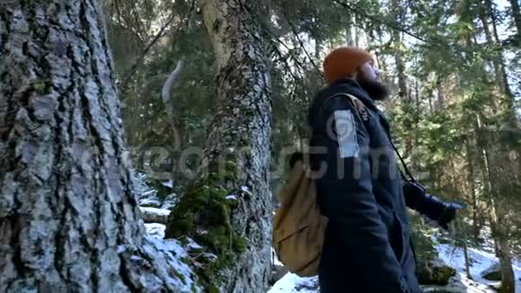一位留着胡子的男性旅行者摄影师在冬天的森林里用他的相机拍摄大自然的照片旅行概念视频的预览图