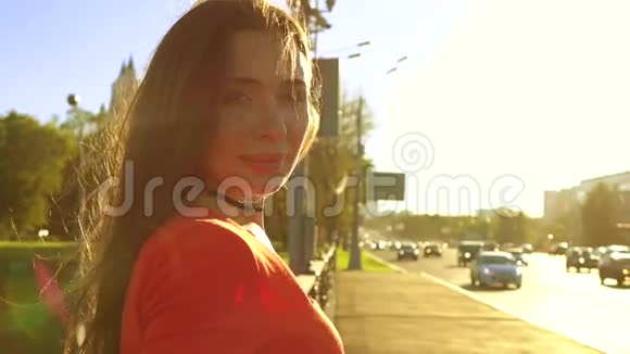 快乐的黑发女孩穿着红色的裙子站在阳光明媚的街道上温暖的晚色慢镜头视频的预览图