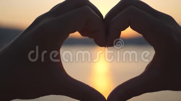 年轻女性手的剪影使心脏形状在海洋背景与美丽的日落夏季概念视频的预览图