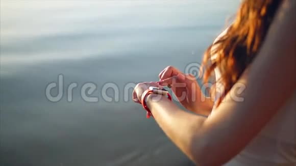 在靠近海边的海滩上用智能手表近距离拍摄女人的手视频的预览图