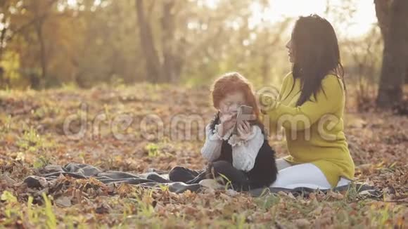 美丽的年轻母亲和她可爱的红头女儿在秋天的公园里玩得很开心母亲照顾她的女儿视频的预览图