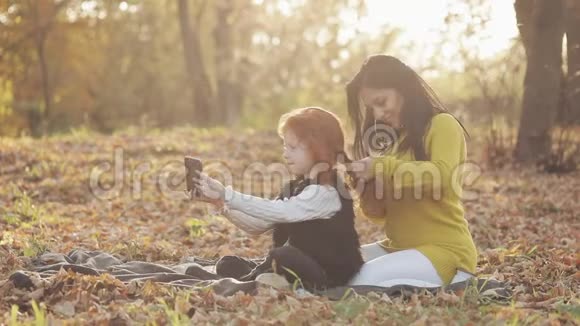 美丽的年轻母亲和她可爱的红头女儿在秋天的公园里玩得很开心母亲照顾她的女儿视频的预览图