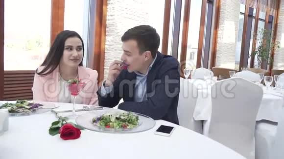一对情侣在餐馆吃晚饭一个男人用一个浆果在亲吻中喂一个女孩慢动作股票录像视频的预览图