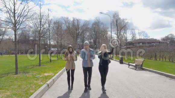 年轻人一个男人和两个女孩在公园里散步打电话晴天好视频的预览图