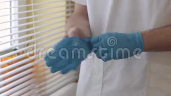 特写医生戴上蓝色消毒乳胶手套男医生站在窗口附近的医疗办公室视频的预览图