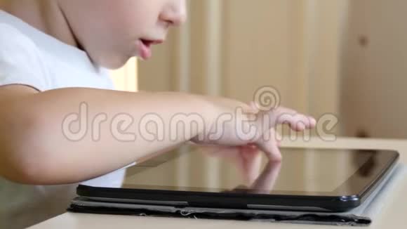 坐在桌边的小男孩摸着平板电脑的触摸屏一个孩子在玩平板电脑视频的预览图