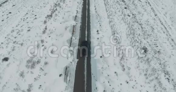 黑车在雪林的冬季乡间小路上行驶从无人驾驶飞机上俯瞰空中景色视频的预览图