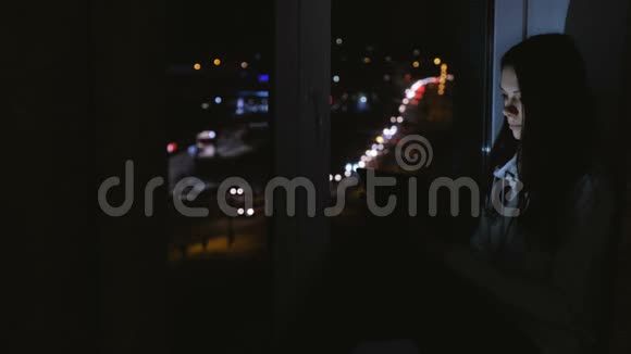 在黑暗的夜晚女人坐在窗台上用平板电脑浏览网页道路背景视频的预览图