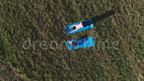 在温暖的夏日里妈妈和她的小女儿在田野上的垫子上伸展空中全景视频的预览图