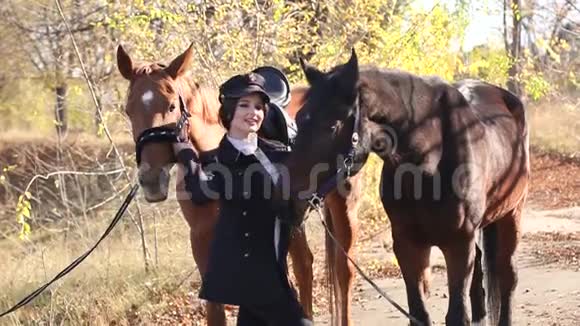 在温暖的秋天天气里活泼的小女孩带着两匹马在森林里散步视频的预览图
