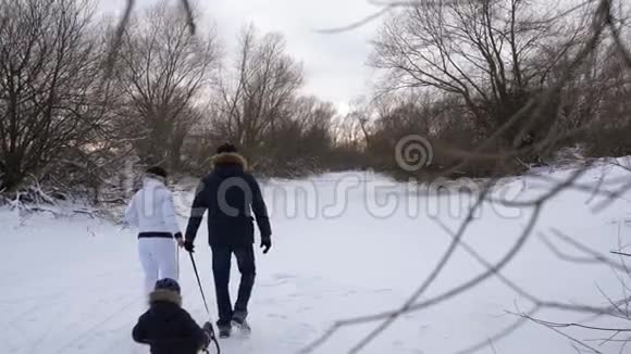 快乐的父母在拉着雪橇的小儿子时走得很远同时捕获的长子欢乐的家庭视频的预览图