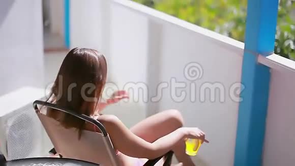 坐在酒店夏季阳台椅子上的白人女孩视频的预览图
