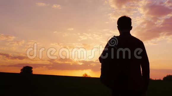 一个背着背包的少年在田野里或乡村里走向日落剪影视频的预览图