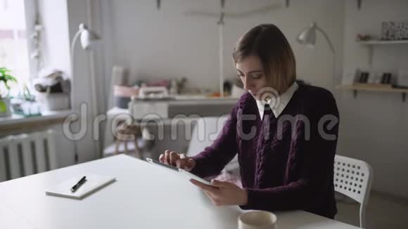 年轻女子坐在家里的桌子上用平板电脑视频的预览图