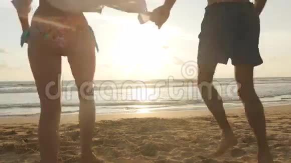 年轻夫妇正在海滩上跑步男人在日落时拥抱和旋转他的女人女孩跳到男友怀里视频的预览图