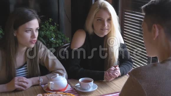 两个女孩和一个年轻人坐在一张桌子旁的咖啡馆里说话他们喝茶吃披萨他们告诉新闻他们视频的预览图