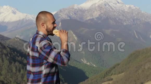英俊的秃头远足者在大自然中在美丽的山景中吃面包视频的预览图