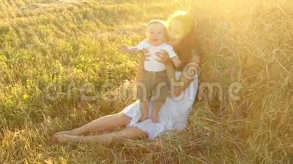 穿着白色衬衫的孩子坐在干草堆附近的年轻母亲穿着白色连衣裙视频的预览图